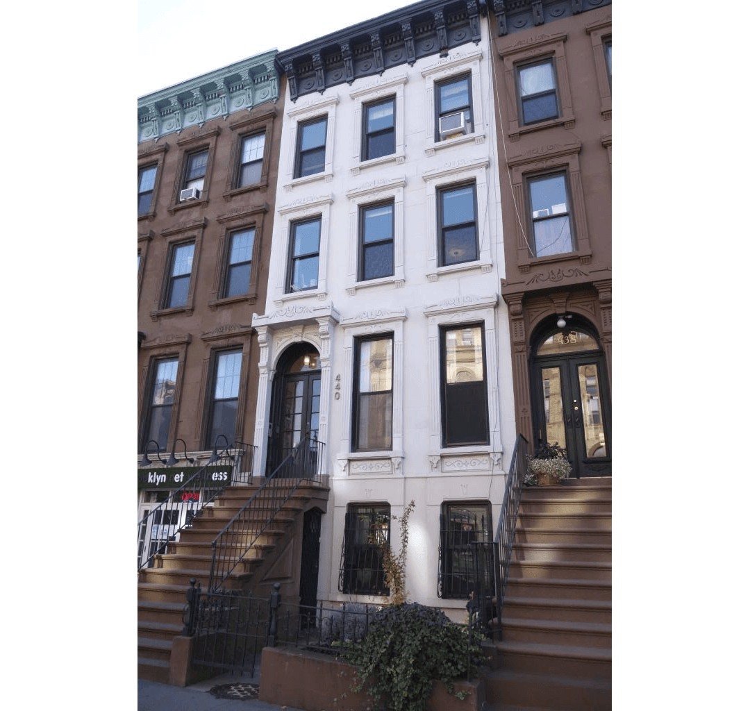 white exterior of the brownstone with a stoop and a bracketed cornice