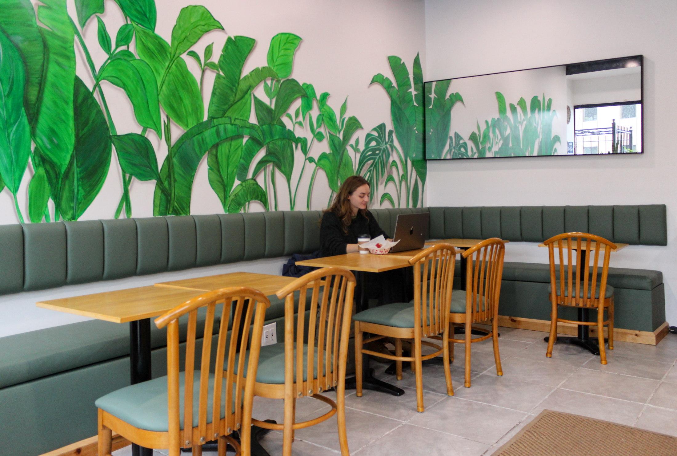 person sitting in a green upholstered booth with wall behind painted with leaves