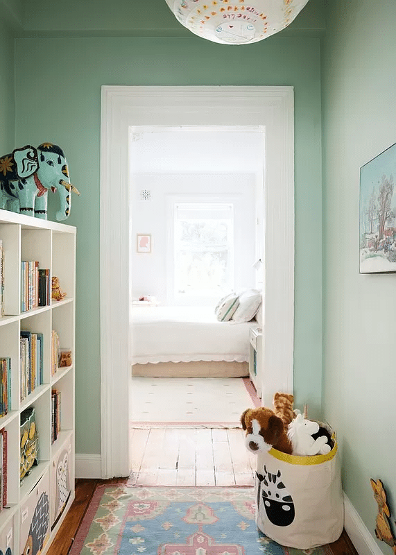 windowless play room with pale green walls, view into a bedroom