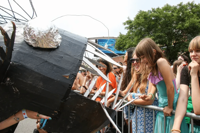 A cardboard anglerfish gets to know a young parade guest