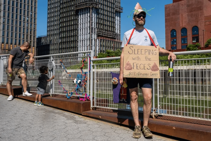 person with cardboard sign saying sleeping with the feces