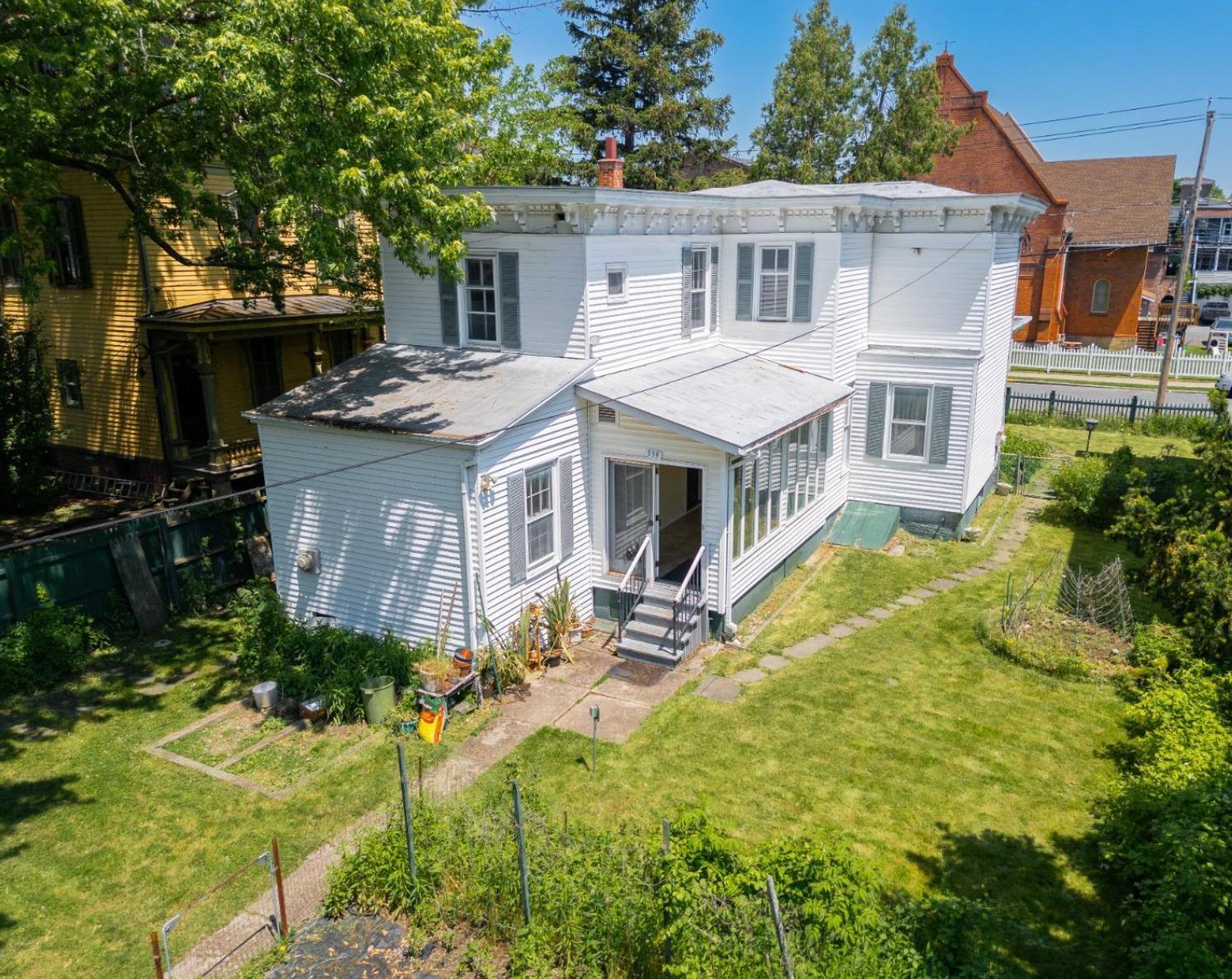 aerial view of the rear facade of the white clapboard house a rear entrance and a fenced-in yard