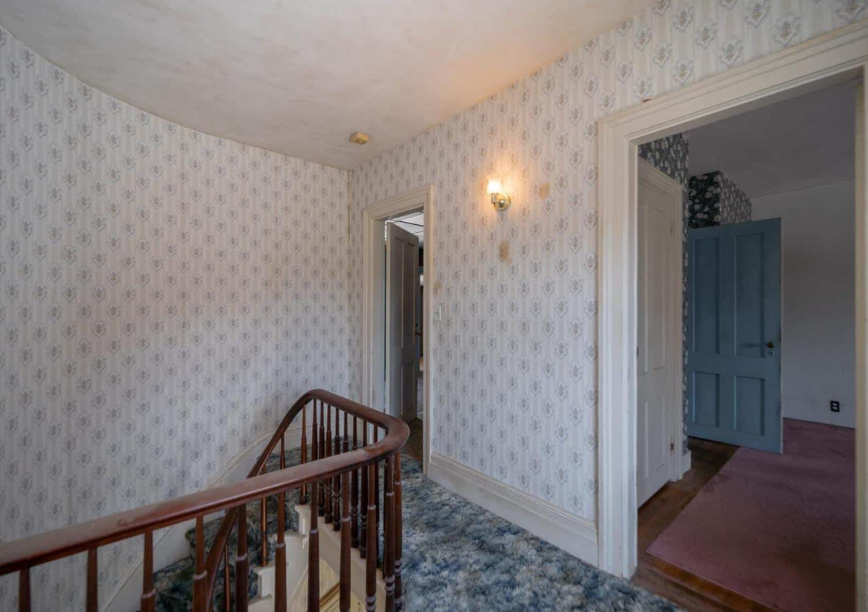 upstairs hallway with curved rail of stair, wallpaper, and carpeting