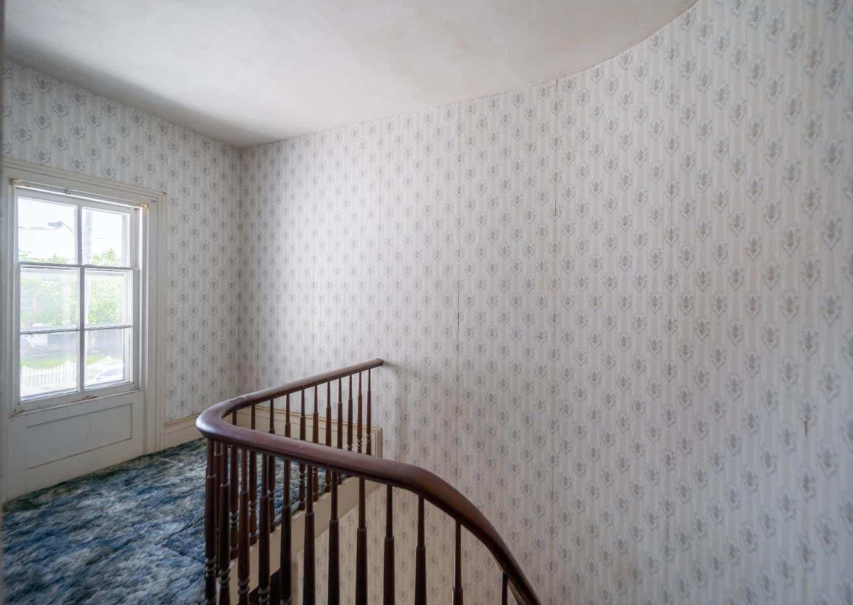 upstairs hallway with curved rail of stair, wallpaper, and carpeting