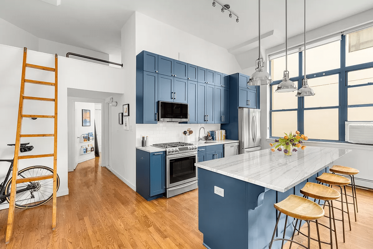 A kitchen with a marble-top island, bar seating, and blue upper and lower cabinets.