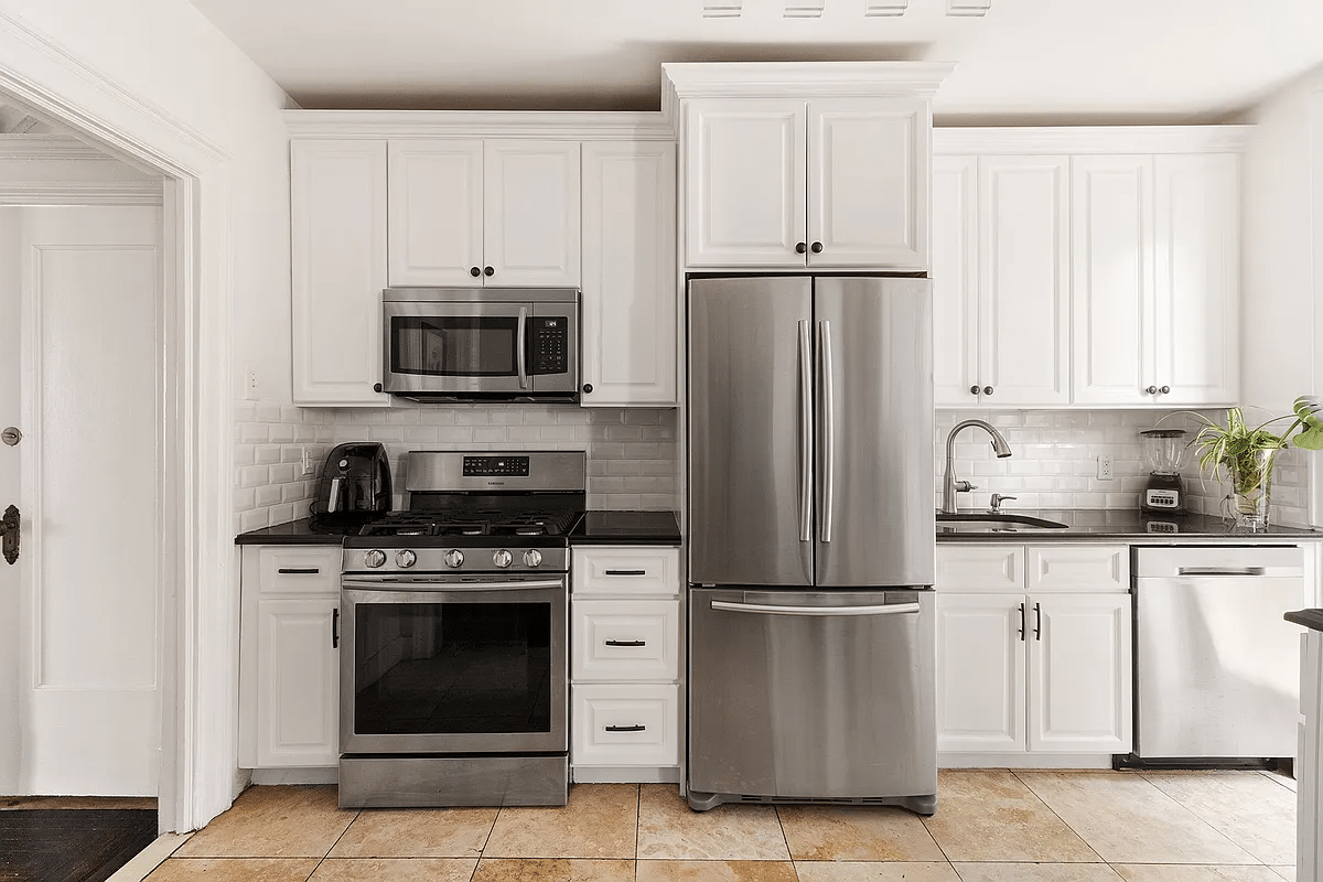 Kitchen with white cabinets, stainless steel appliances and beige floor tiles