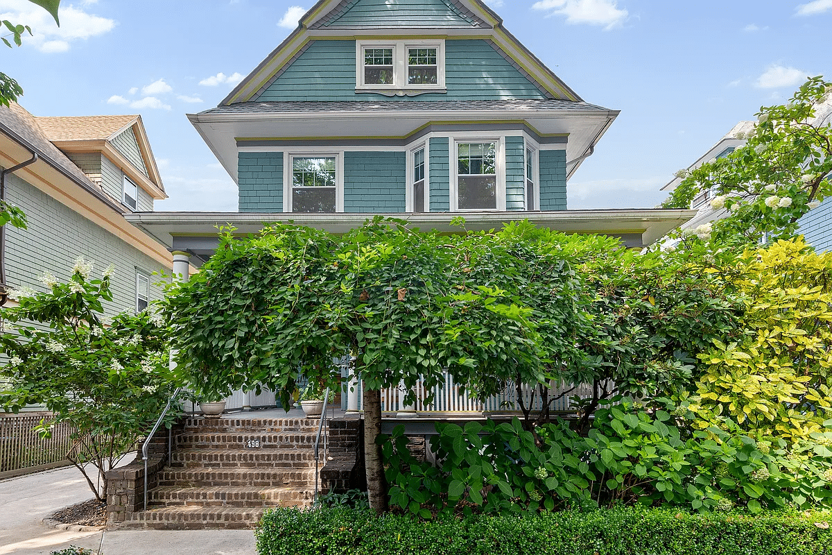 blue house with a front porch hidden by a tree and shrubbery