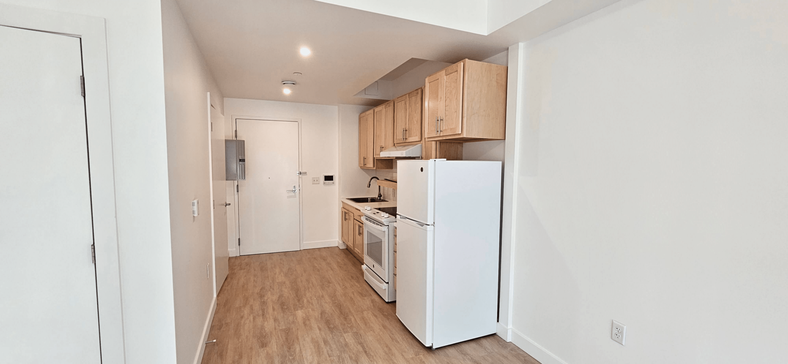 one wall kitchen with wood cabinets near the apartment entrance