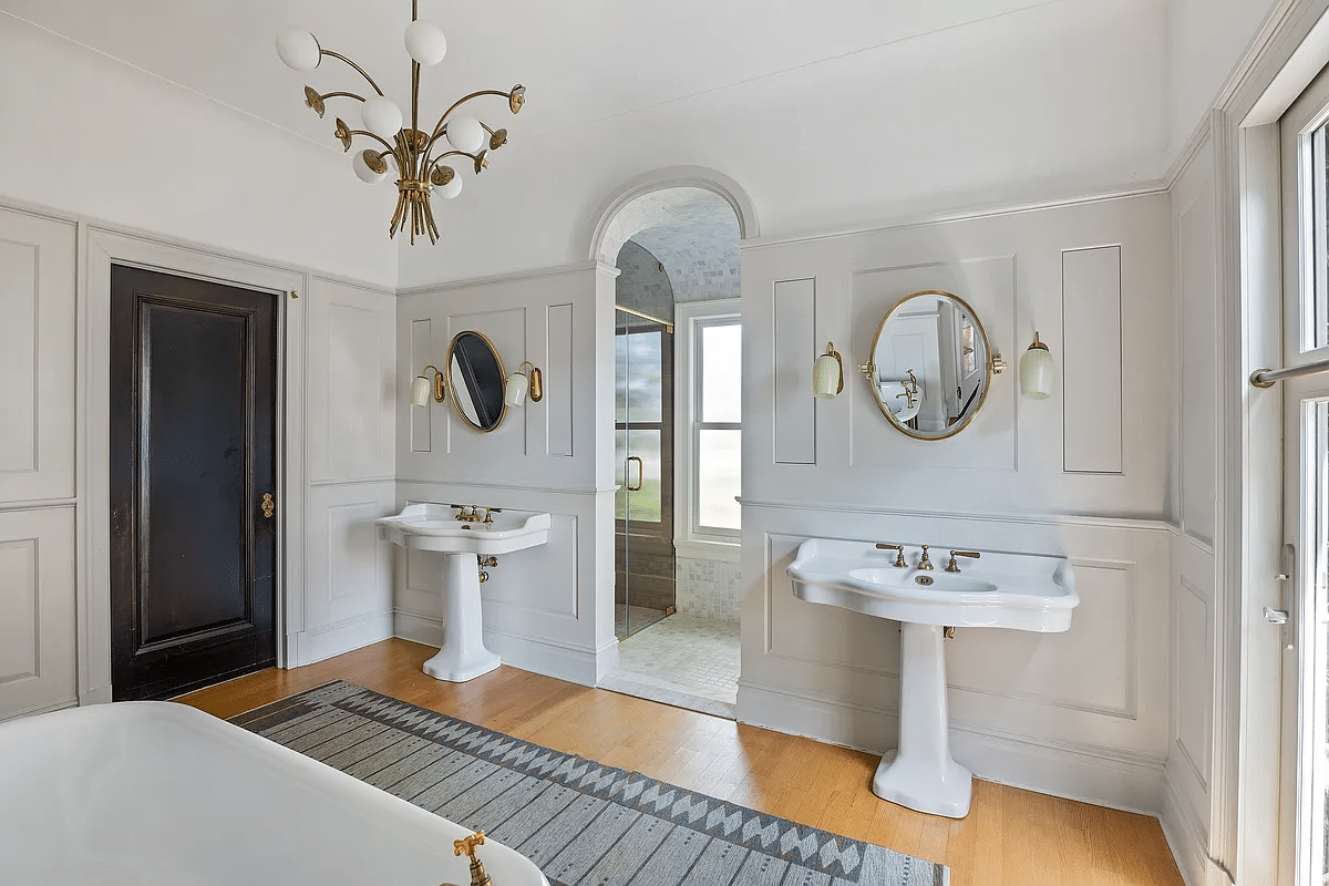 bathroom with two pedestal sinks, wood floor, free standing tub