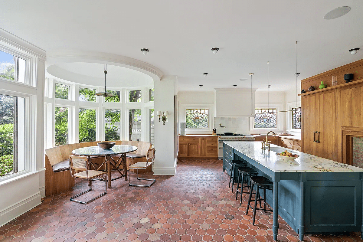 kitchen with large marble topped island, terra cotta tile floor and view to breakfast nook with curved banquette