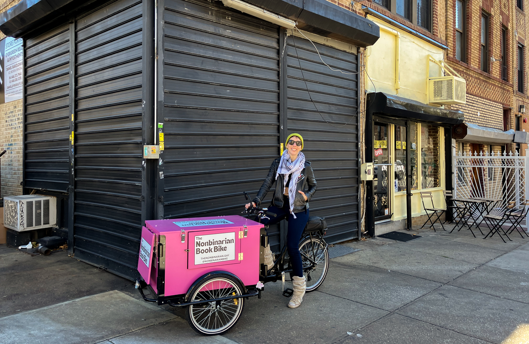 K. Kerimian atop a bike and in front of the gates covering the new bookstore space