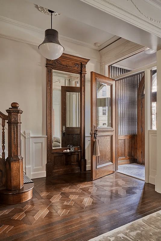 entry with mirror, newel post, wood floor and view to wainscoting in vestibule