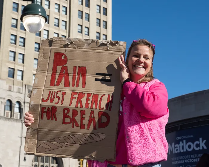 person in pink coat holding a sign "pain just french for bread"