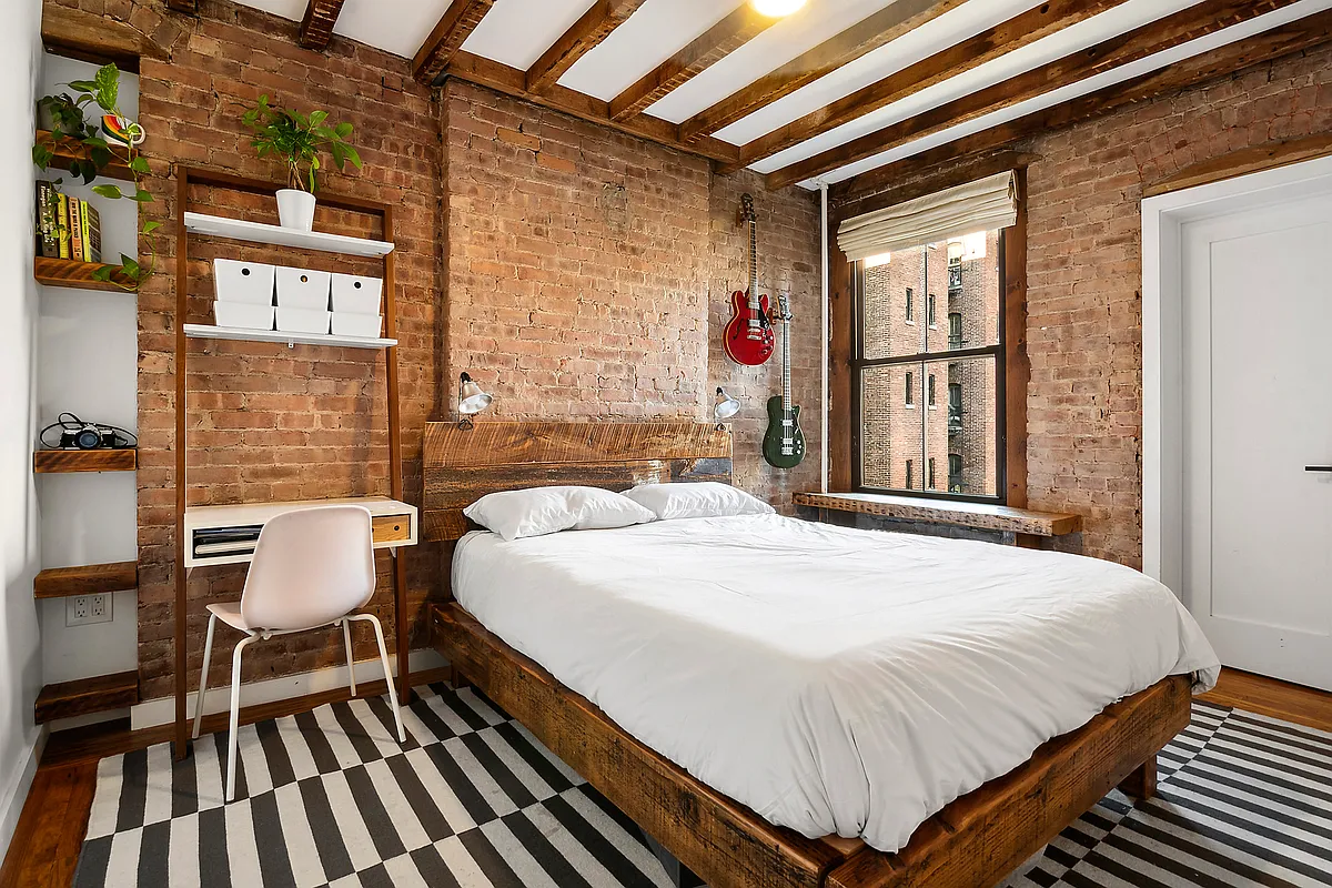 bedroom with exposed brick walls, exposed rafters and a window