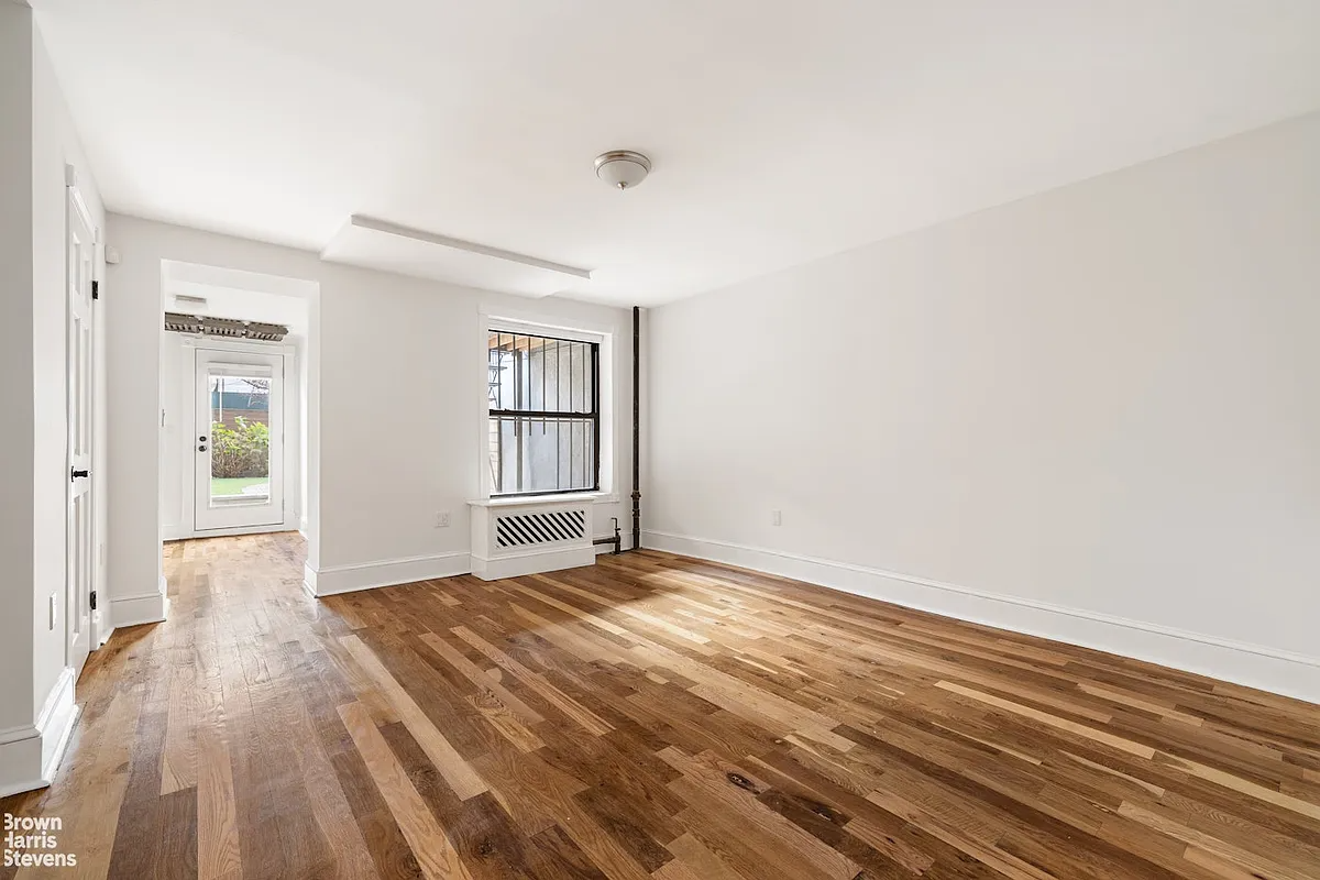 garden level bedroom with white walls, wood floor and access to the rear yard