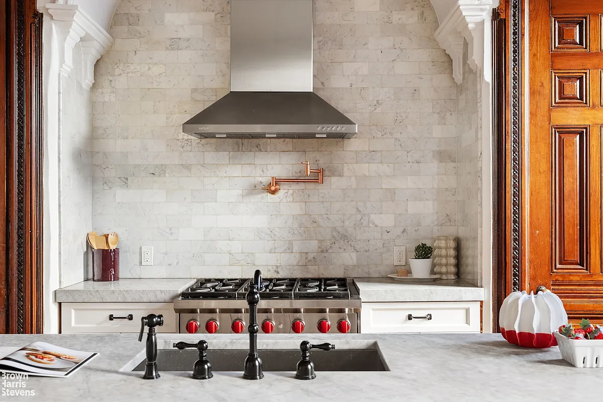 detail of kitchen with cabinets and stove set into a nook with a stainless steel hood